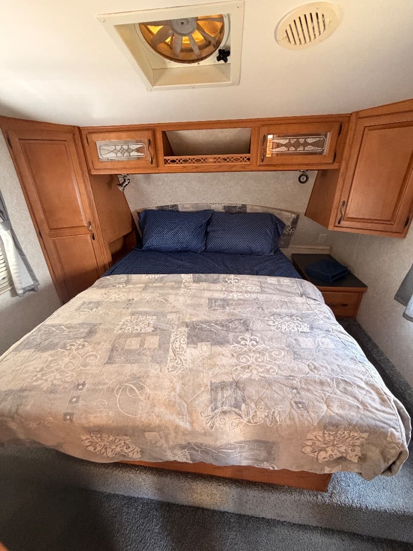 The private front bedroom of The Quantum with a made-up queen bed, overhead cabinets, a wardrobe and a roof vent fan