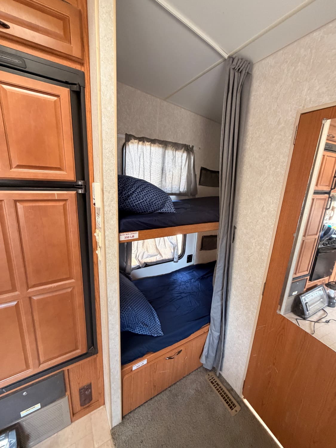 Two bunk beds in The Quantum, made up with bedding and closed off by their own privacy curtain, beside the refrigerator