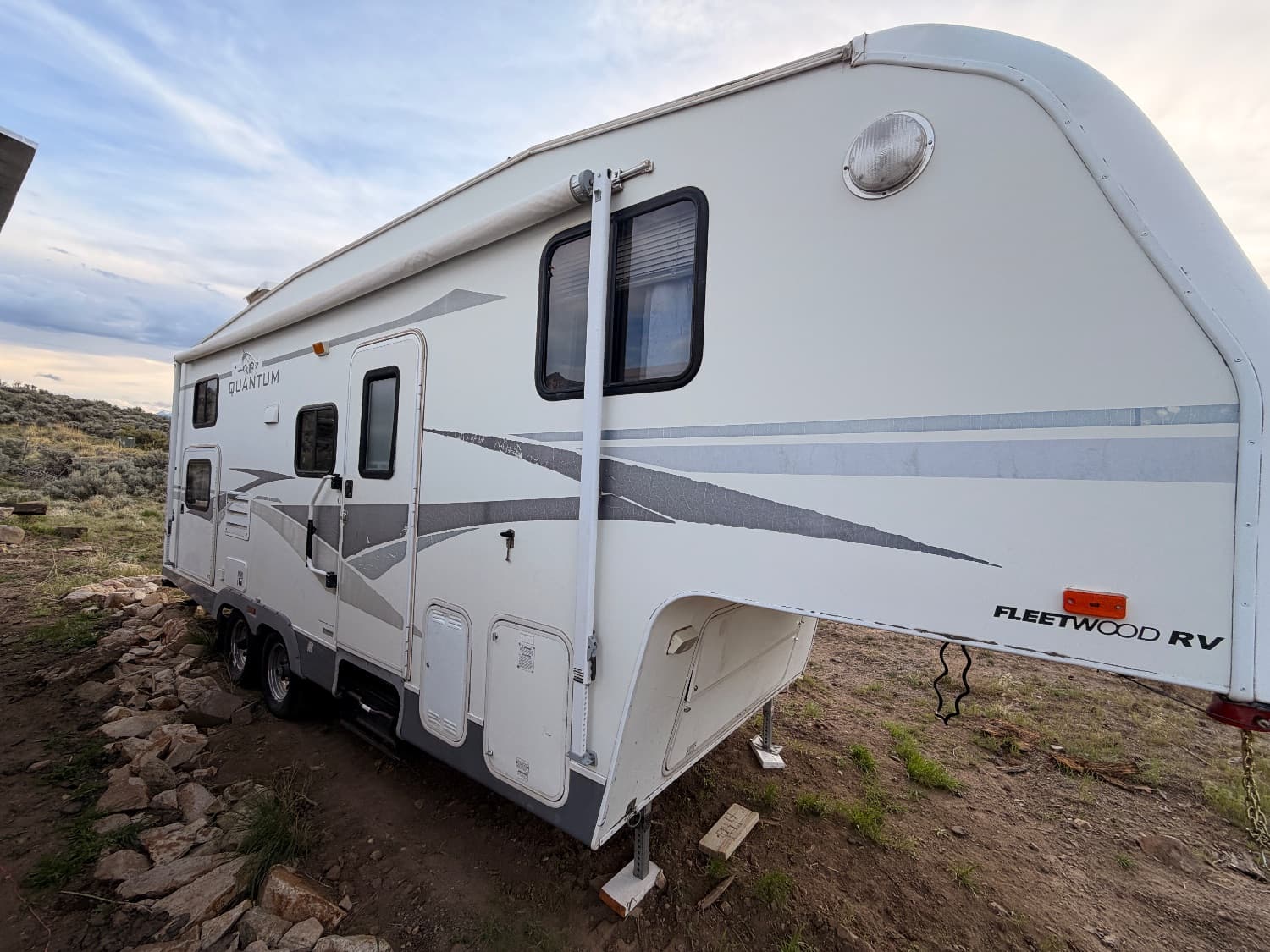 Side view of The Quantum fifth wheel showing the entry door, tandem axles and exterior storage compartments