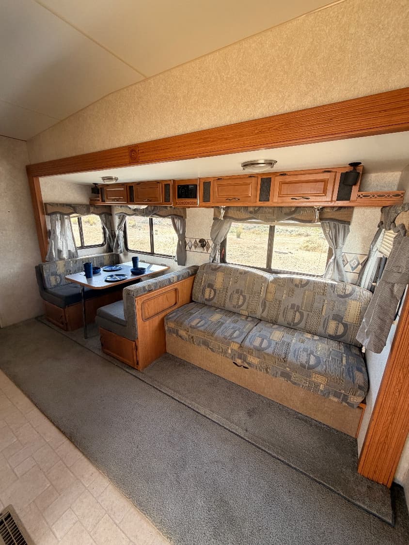 The main living area of The Quantum with a dinette booth set for a meal and a sofa along the wall, windows looking out over open desert