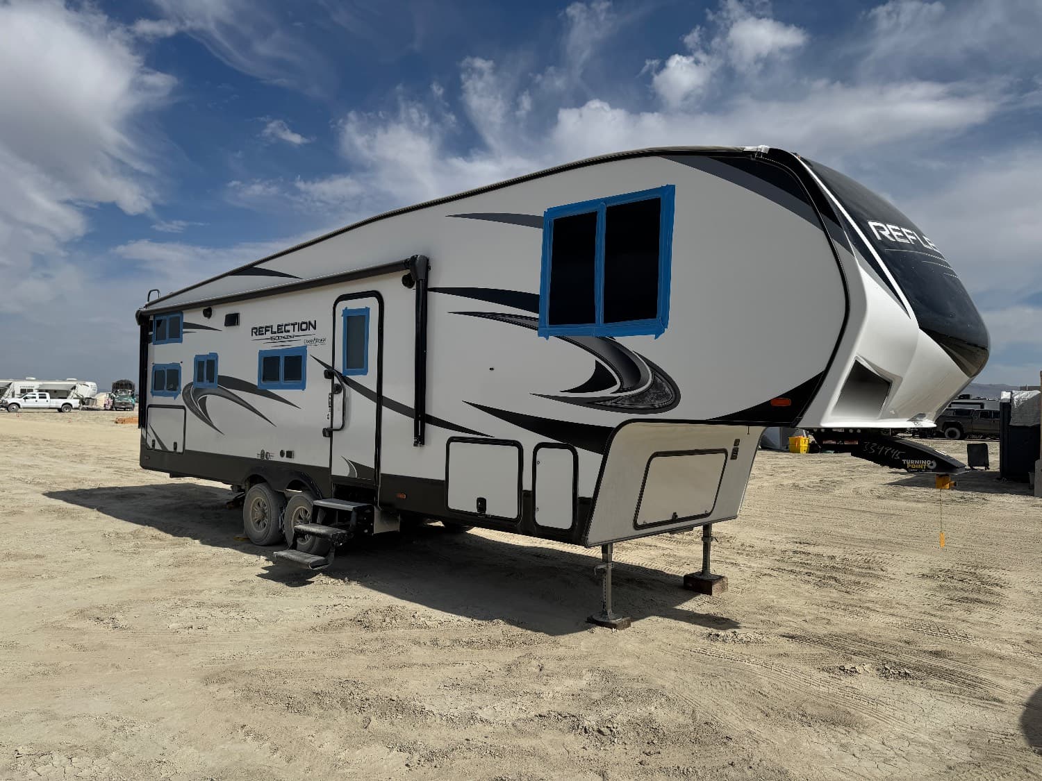 The Reflection, a white and grey Grand Design Reflection fifth wheel, set up and levelled on the playa with its windows taped and sealed against dust